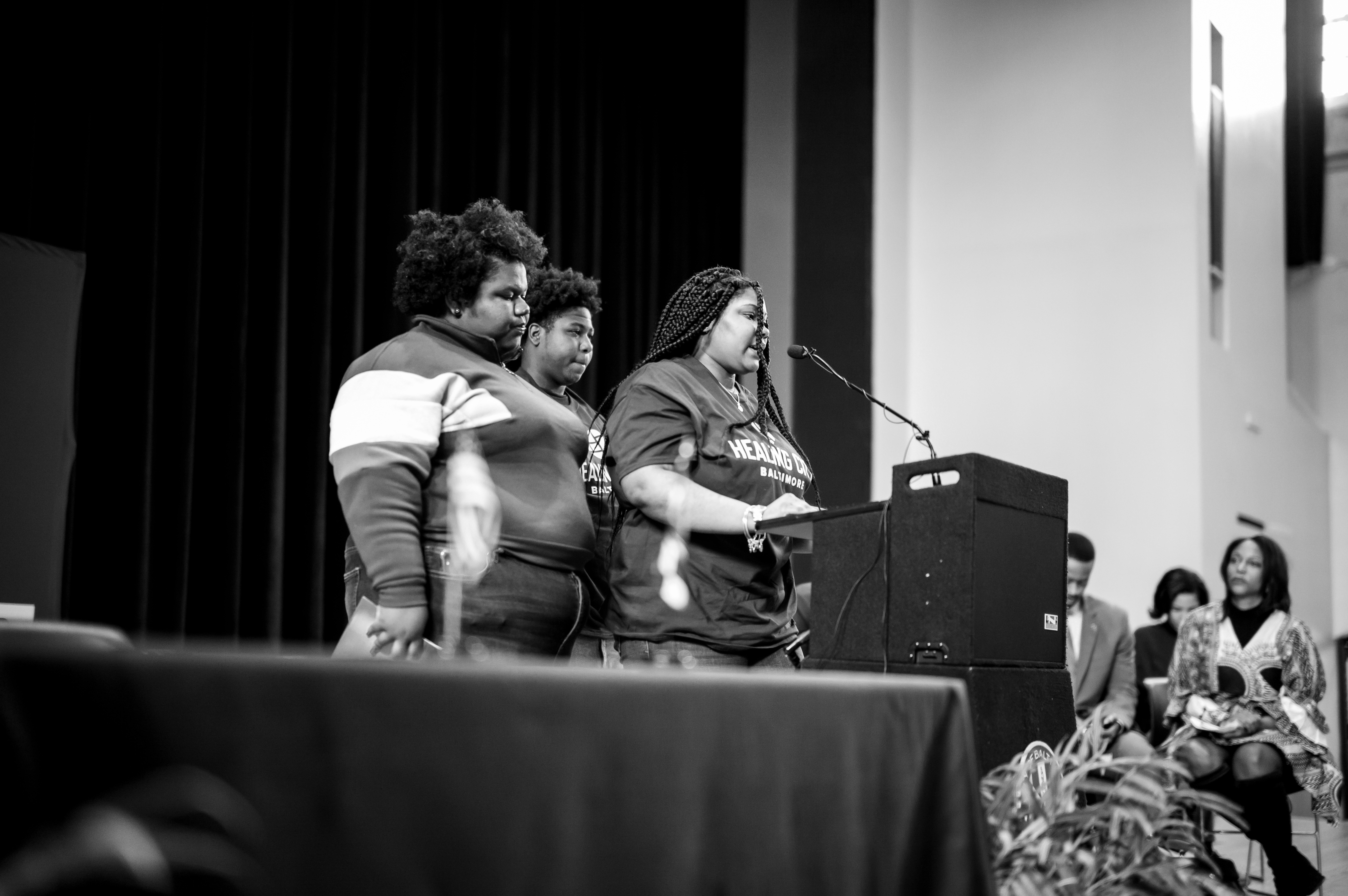Students Bryonna Harris and Jaionna Santos and Damani Thomas, who initially called on the Baltimore City Council to address trauma in Baltimore, speak at the signing of the Elijah Cummings Healing City Act. Photo by John Waire, thewairehouse.com; used with permission.